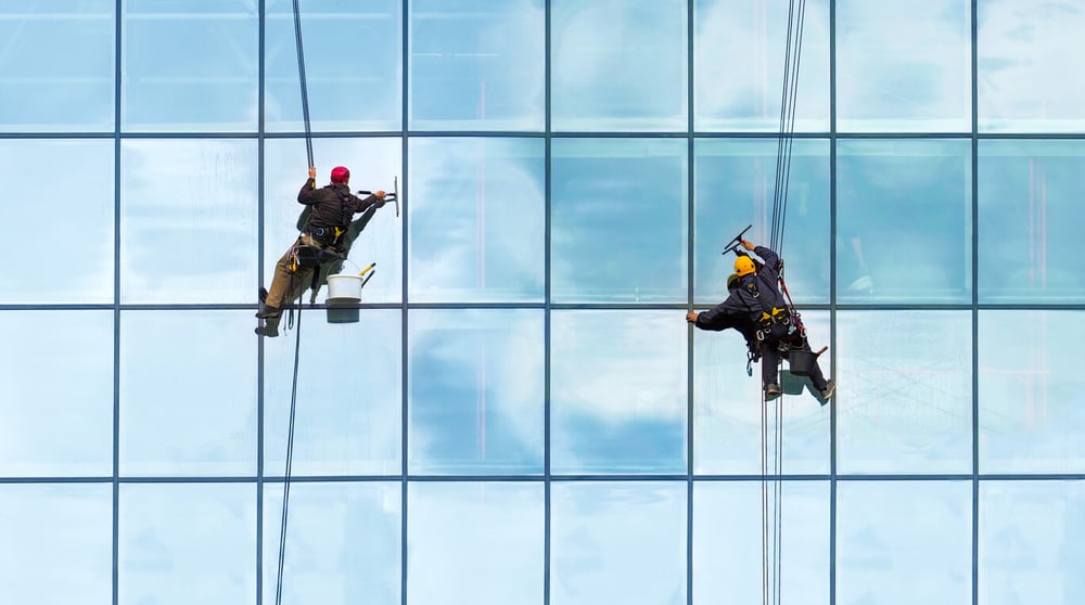 A professional window cleaner using a squeegee on a high-rise building, covered by window cleaning insurance for general liability protection.